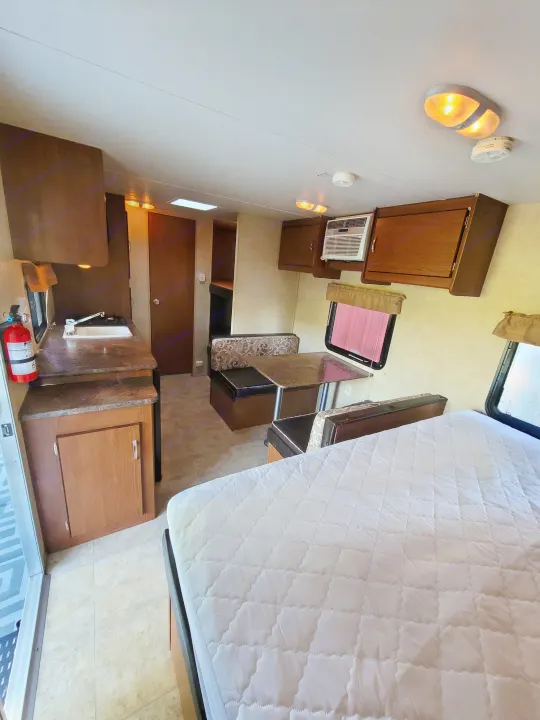 Bright RV rental interior with a kitchenette, dinette, bed, and overhead storage. Ideal for travel.. Forest River Wildwood X-Lite 2014