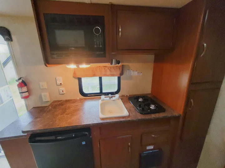 Well-equipped RV rental kitchen featuring microwave, sink, two-burner stove, and small fridge.. Forest River Wildwood X-Lite 2014