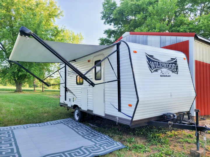 Wildwood travel trailer RV rental with extended awning for outdoor camping. Parked on grass by a red barn.. Forest River Wildwood X-Lite 2014