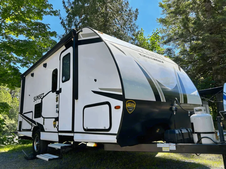 White Sunset Trail Super Lite travel trailer, a perfect rv rental for camping trips, parked among tall trees.. Sunset Trail 188BH 2022