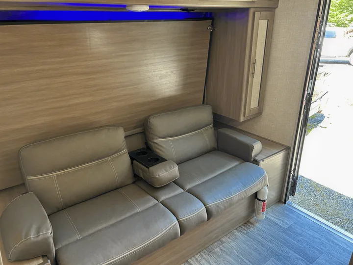 Modern RV rental interior featuring a gray sofa with cup holders, wall panel, blue LED lighting, and fire extinguisher.. Sunset Trail 188BH 2022