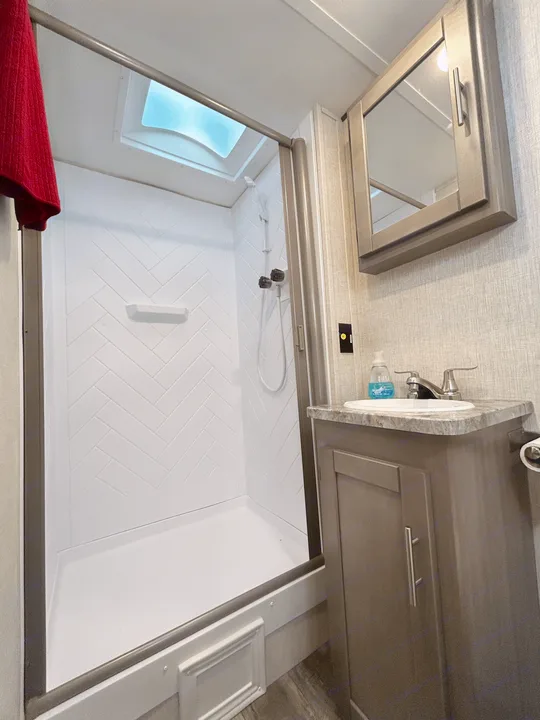 Modern RV rental bathroom with a spacious walk-in shower featuring herringbone walls and a skylight, plus a stylish vanity.. Sunset Trail 188BH 2022