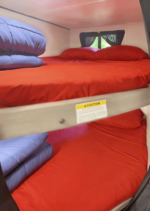 RV rental sleeping area: bunk beds with bright red sheets, blue comforters, and a safety caution label.. Sunset Trail 188BH 2022