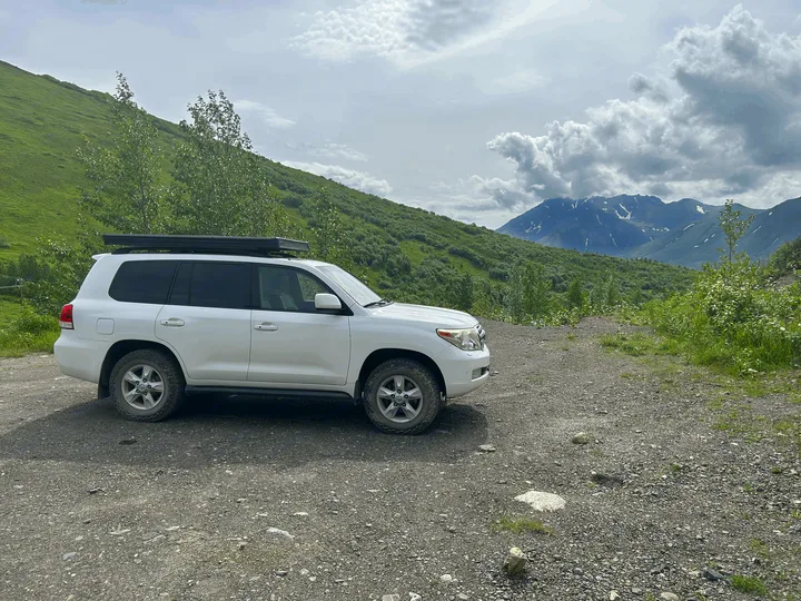 White SUV with roof rack on a gravel mountain path, ideal for outdoor exploration or an rv rental adventure.. Toyota Land Cruiser 2008