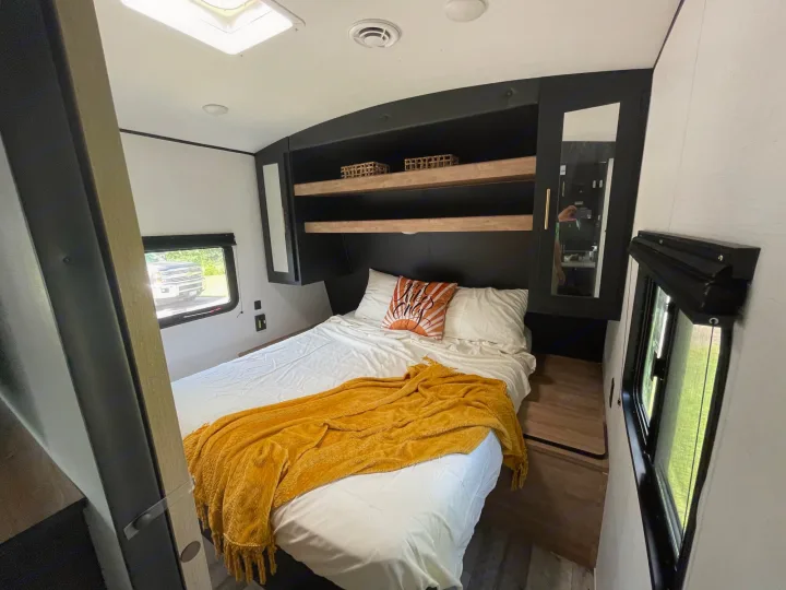 Modern RV rental bedroom featuring a queen bed, cozy yellow throw, and smart overhead storage.. Keystone RV Springdale 2023