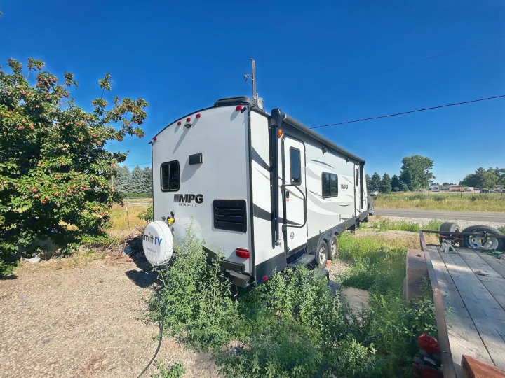 A gray and white MPG Ultra-Lite RV, ideal for an rv rental trip, sits parked among green foliage and gravel under blue sky.. Cruiser Rv Corp 2450RK 2019