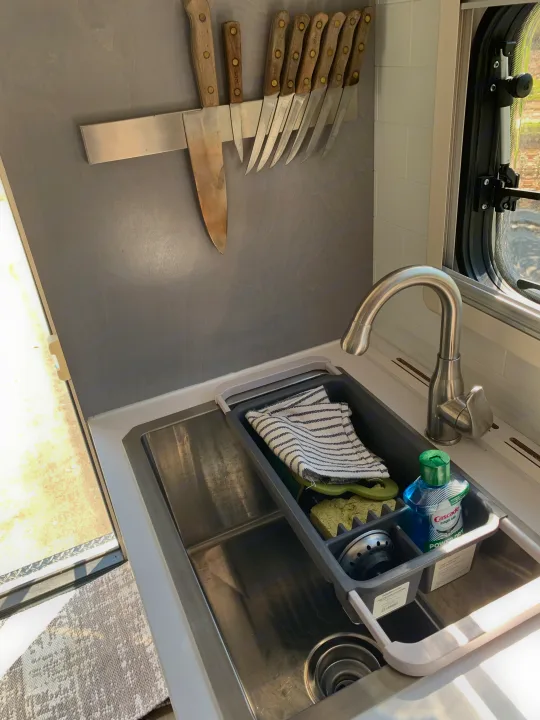 Compact RV rental kitchen features a stainless steel sink with a dish drainer, faucet, and magnetic knife rack above.. Ford F350 Diesel Double Cab 2020
