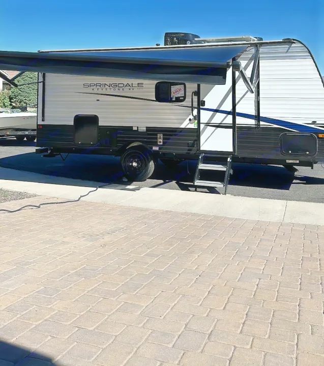 This white and black Springdale travel trailer, ideal for your next rv rental adventure, shows an extended awning and steps.. Keystone RV Springdale 2023