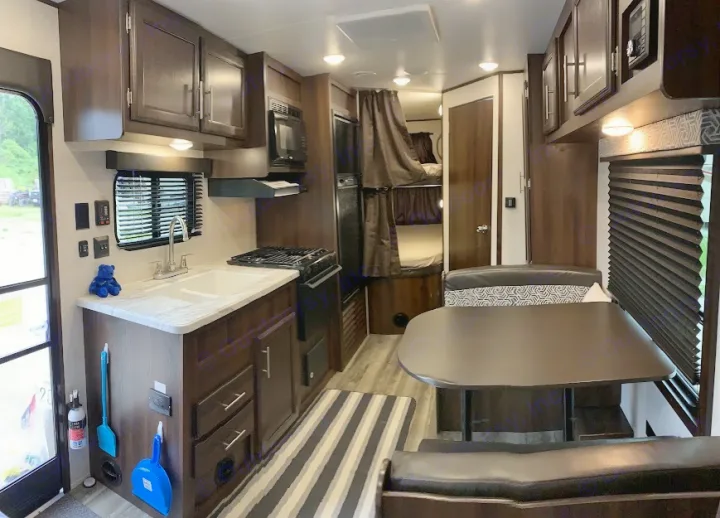 Spacious RV rental interior: kitchen with sink & stove, dining booth, and bunk beds. Features dark wood, light walls.. Jayco Jay Flight SLX 2019