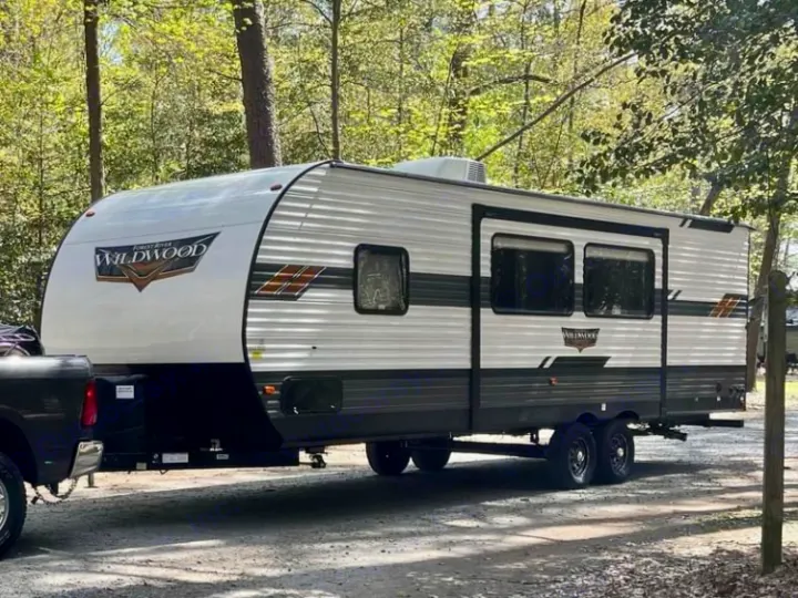 RV rental: A white and grey Wildwood travel trailer hitched to a truck, ready for camping in a wooded site.. Forest River Wildwood 2021