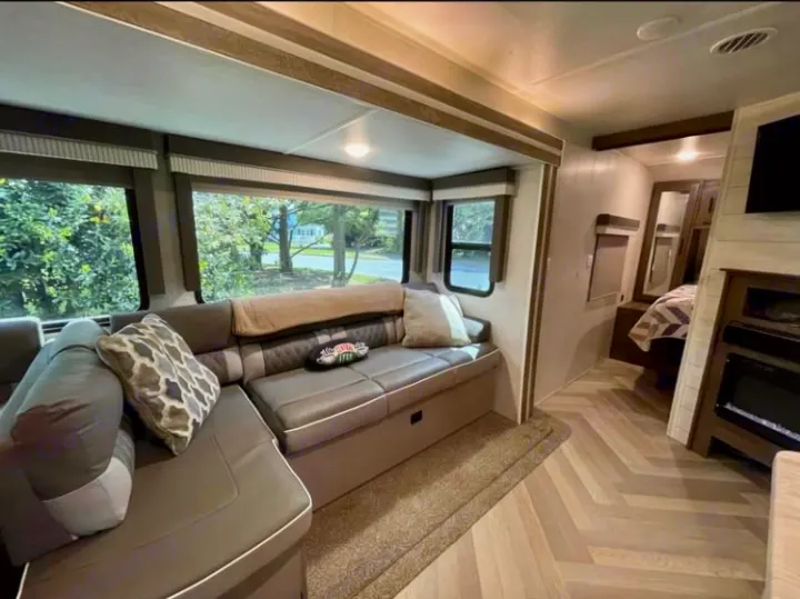 Modern RV rental interior: spacious living area with comfy L-shaped sofa & bedroom view.. Forest River Wildwood 2021