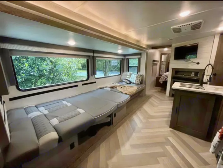 Modern RV rental interior with spacious living area, convertible seating, kitchen, and light herringbone floors.. Forest River Wildwood 2021