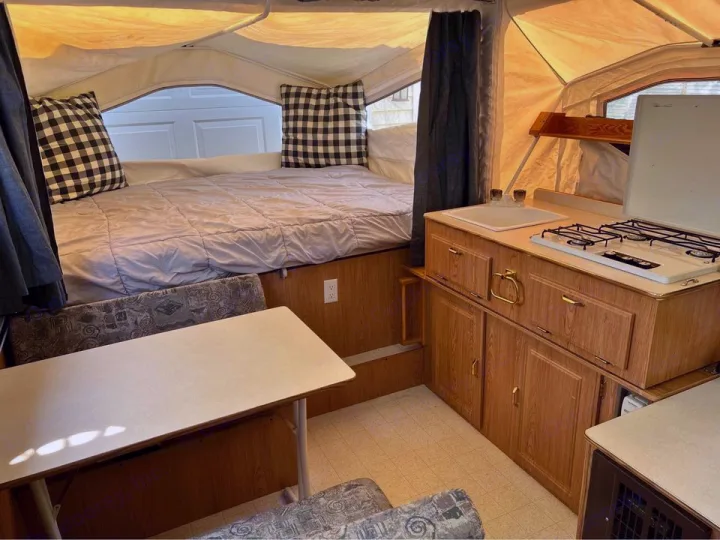 Interior of a well-maintained pop-up RV rental, featuring a cozy bed, compact kitchen, and dining area.. Forest River Rockwood Premier 2004