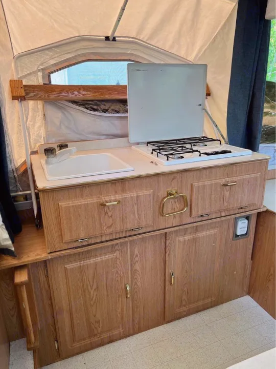 Inside an RV rental: a compact kitchen area with a white sink, 2-burner stove, and light wood cabinets.. Forest River Rockwood Premier 2004