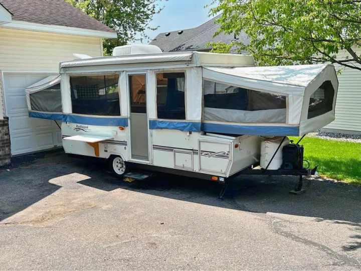 White pop-up camper RV rental set up in a sunny driveway with extended canvas bunks and a side table.. Forest River Rockwood Premier 2004