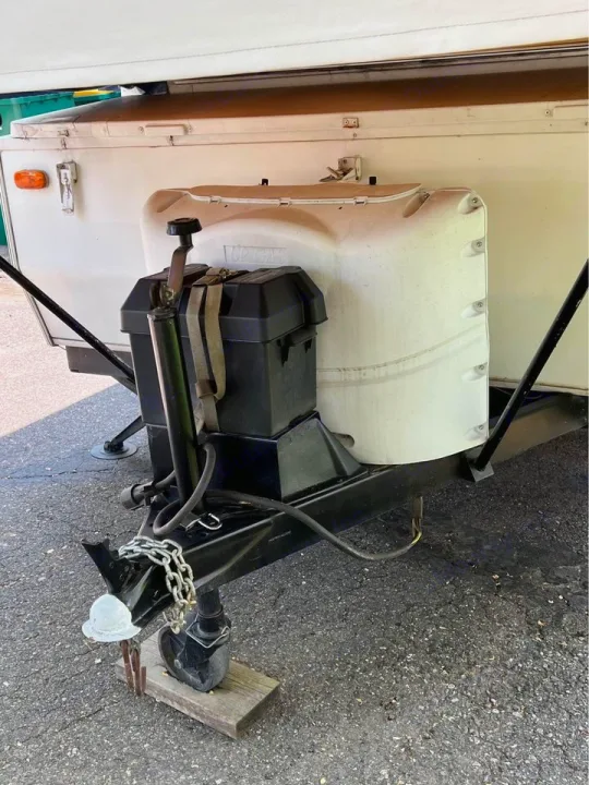 RV rental: Front view of a pop-up camper's hitch, showing propane tank, battery box, and tongue jack on asphalt.. Forest River Rockwood Premier 2004