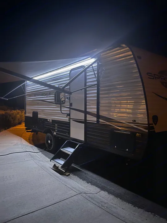 Brightly lit rv rental at night, showing extended awning & steps. Ready for travel!. Keystone RV Springdale 2023