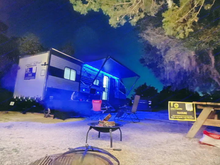 Nighttime RV rental scene: blue lights, fire pit, and camping chairs. Ready for a nature escape.. Forest River Wolf Pup 2021