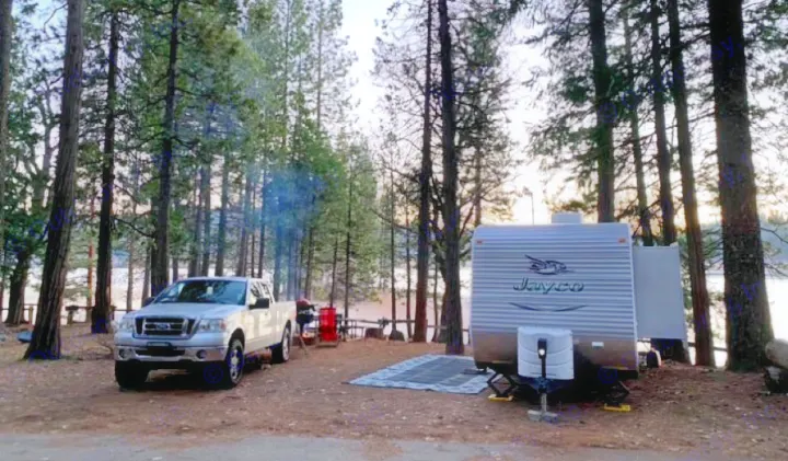 RV rental and pickup truck campsite setup by a lake in a pine forest, with smoke from a fire.. Jayco Jay Flight 2015