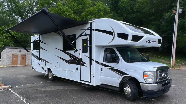 White Jayco Class C RV rental, parked with black awning extended. Ideal for camping and travel adventures.. Jayco Redhawk 31F 2024