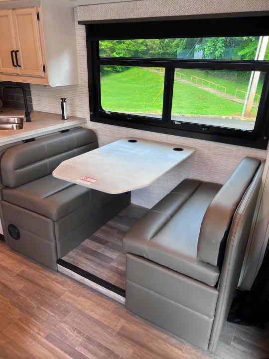RV rental: Cozy interior featuring a gray dinette booth, light table, and kitchen counter, by a large window with outdoor views.. Jayco Redhawk 31F 2024