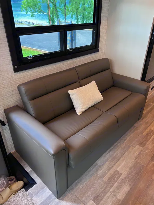 RV rental's inviting living area with a plush gray sofa, white pillow, and large window overlooking a lake.. Jayco Redhawk 31F 2024