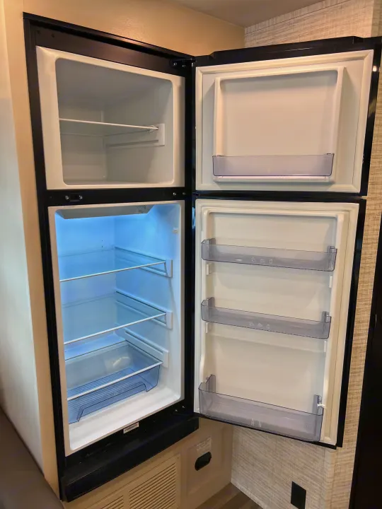 Open two-door refrigerator and freezer in an RV rental, revealing clean white interior with shelves and clear door bins.. Jayco Redhawk 31F 2024