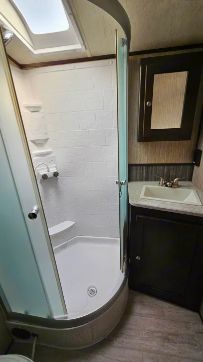 RV rental bathroom features: clear glass shower enclosure, white tiled walls, curved base, sink, and dark cabinetry.. Cruiser RV Shadow Cruiser 2019