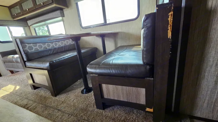 RV rental interior: A dinette features dark brown upholstered benches and a table. Visible wear on wood trim near windows.. Cruiser RV Shadow Cruiser 2019