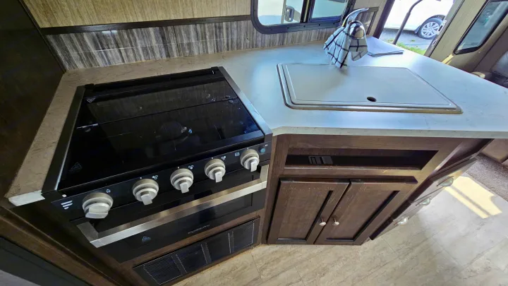 RV rental kitchen featuring a black stovetop, oven, white sink, and brown cabinetry, ideal for travel cooking.. Cruiser RV Shadow Cruiser 2019