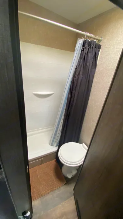 Compact RV rental bathroom featuring a shower with a blue and white curtain, toilet, and bath mat.. Eclipse Recreational Vehicles Attitude 2016