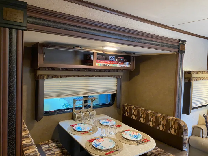Cozy RV rental dinette with a set table, booth seating, and board games in the overhead cabinet.. Jayco Jay Flight 2015