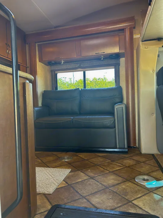 RV rental living area: black sofa, overhead wood cabinets, and a window. Enjoy comfort on your road trip!. Thor Citation 2015