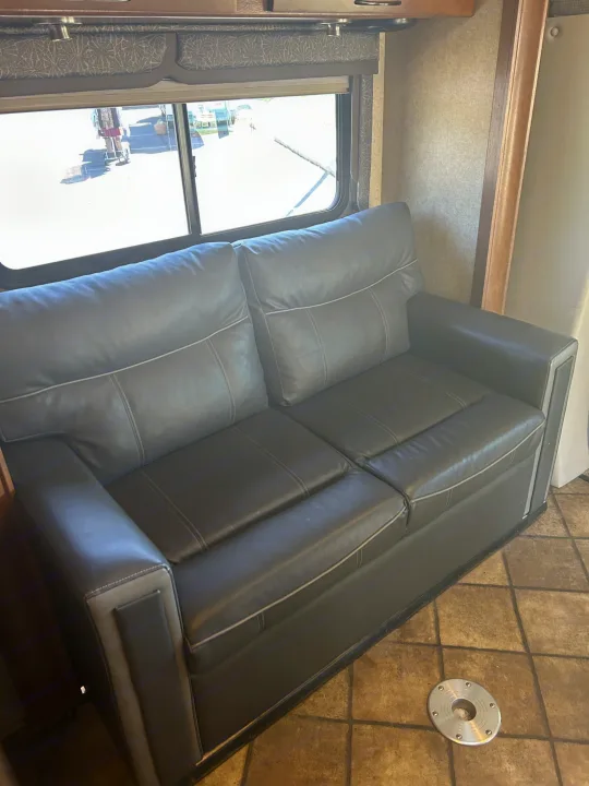 RV rental living area featuring a comfortable dark gray sofa with light piping, large window, and tiled floor.. Thor Citation 2015