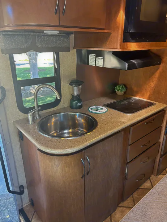 Experience comfort in this RV rental's well-appointed kitchen, featuring a stainless steel sink, cooktop, microwave, and wooden cabinets.. Thor Citation 2015