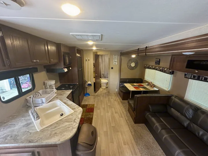Inside this RV rental: kitchen with sink & stove, dining booth, sofa, and bathroom.. Coachmen 264bh 2017