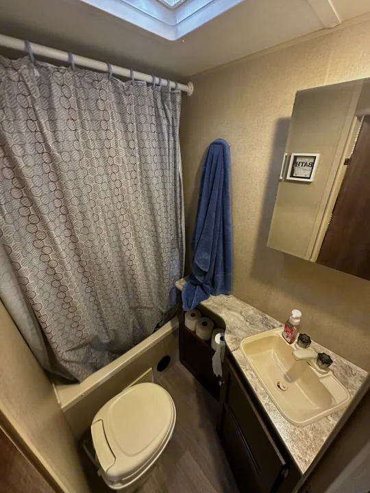 Compact RV rental bathroom: shower with geometric curtain, small toilet, and sink with counter.. Coachmen 264bh 2017