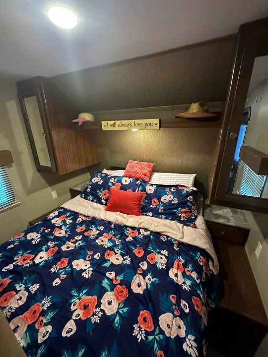 A cozy RV rental bedroom featuring a bed with navy floral bedding, decorative pillows, and overhead storage.. Coachmen 264bh 2017