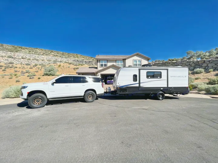 White Chevy Tahoe SUV towing a Springdale RV rental on a sunny street, ready for camping adventures.. Keystone RV Springdale 2023