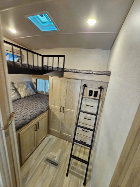 Modern RV rental interior: Bunk bed with ladder, main sleeping area, light wood cabinets & window.. Forest River Flagstaff Super Lite 2022
