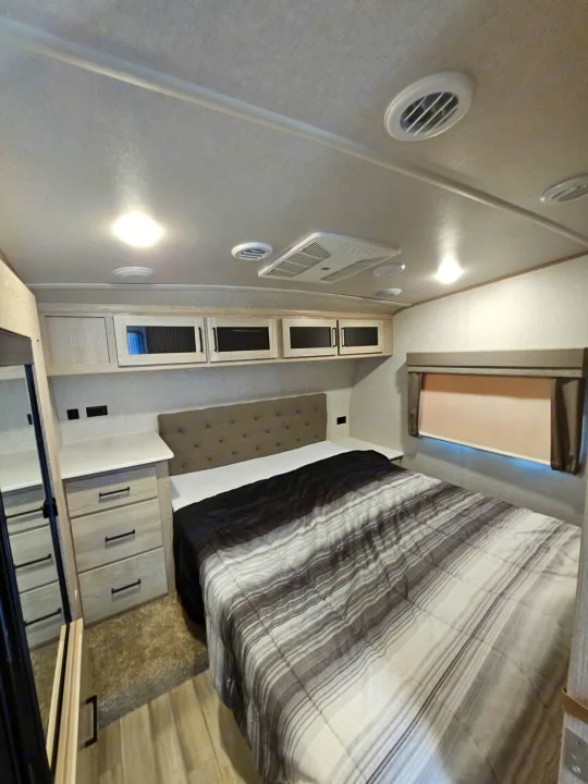Inside a modern RV rental: a cozy bedroom with striped bedding, cabinet storage, and ceiling AC vents.. Forest River Flagstaff Super Lite 2022