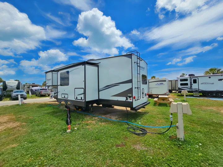 Spacious RV rental at a sunny campground, with hookups visible on the green grass. Other RVs are parked nearby.. Forest River Flagstaff Super Lite 2022