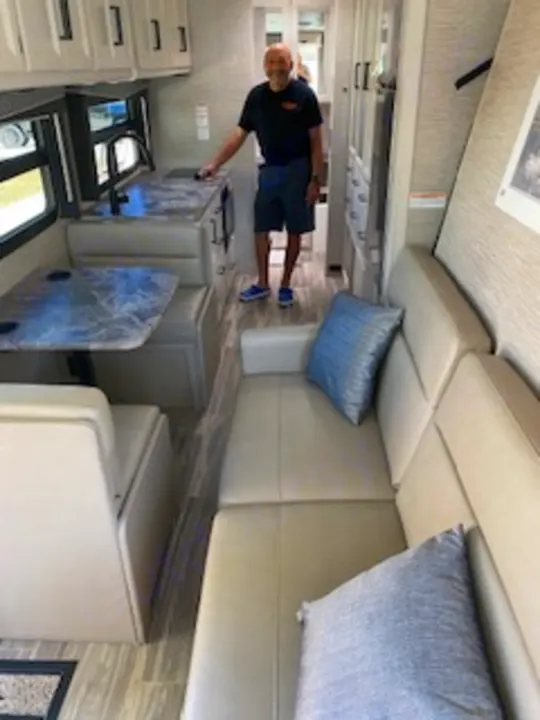 Experience an RV rental! Inside, a man explores a bright, modern interior with kitchen, dining, and lounge areas.. Thor Axis 2023