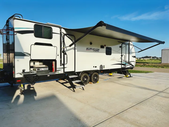 A white Forest River Surveyor Legend RV rental with an extended awning and outdoor kitchen, parked on concrete, ready for adventure.. Forest River Surveyor Legend 2022