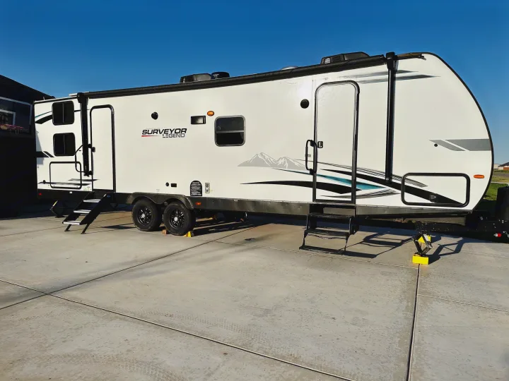 White "Surveyor Legend" travel trailer parked on concrete with steps and jacks, ideal for an rv rental.. Forest River Surveyor Legend 2022