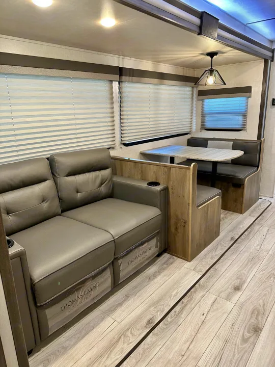 Spacious RV rental interior featuring a comfy gray recliner sofa, dinette, and light wood floors. Perfect for travel.. Forest River Surveyor Legend 2022