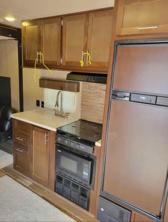 Well-equipped RV rental kitchen featuring a fridge, microwave, stove, sink, and upper cabinets.. Forest River Wolf Pack 2016