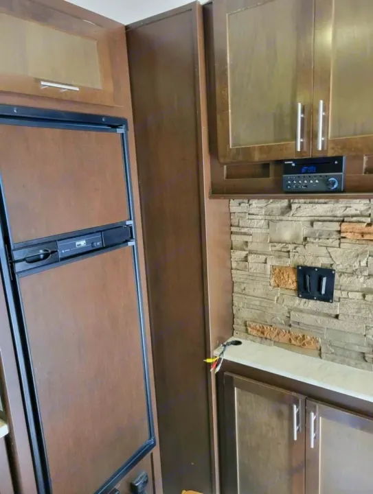 RV rental interior: showing a built-in refrigerator, wood cabinetry, and an entertainment center with a stereo and TV mount.. Forest River Wolf Pack 2016