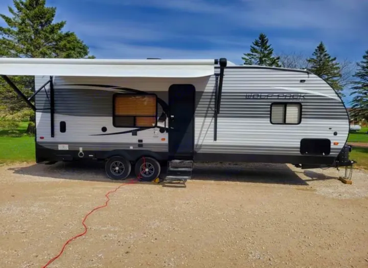 A light gray Wolf Pack travel trailer with an extended awning on a gravel lot, ready for your rv rental getaway.. Forest River Wolf Pack 2016