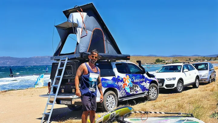 Man by an RV rental truck with a rooftop tent on a sunny beach, ideal for water sports and camping.. Isuzu D-max Double Cab 2020